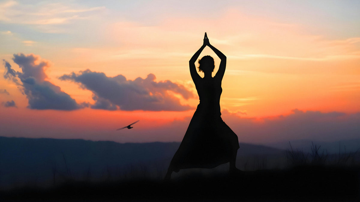 Silohouette of a person practicing yoga in an outdoor setting during sunrise.