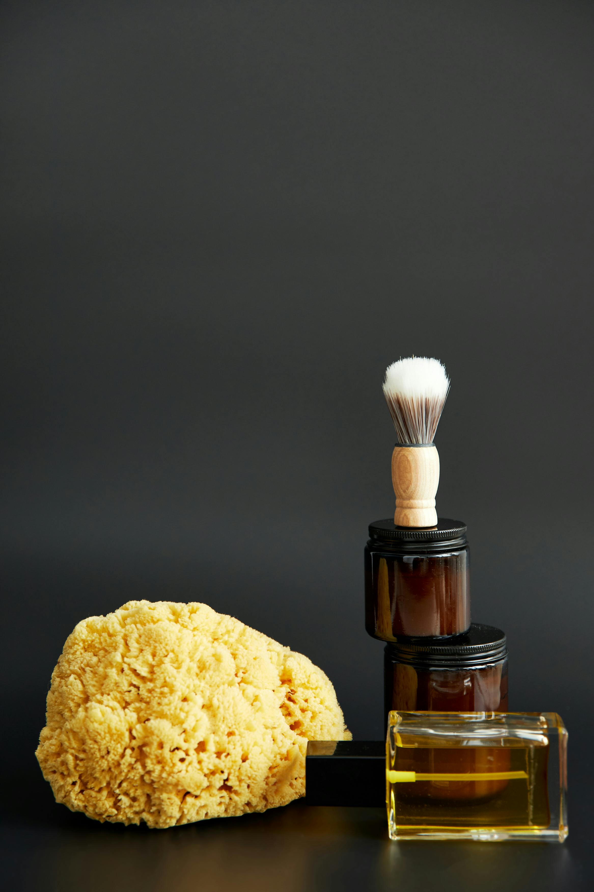 Mens grooming products placed on a counter.  Natural sea sponge, beard balm, aftershave and shaving brush.