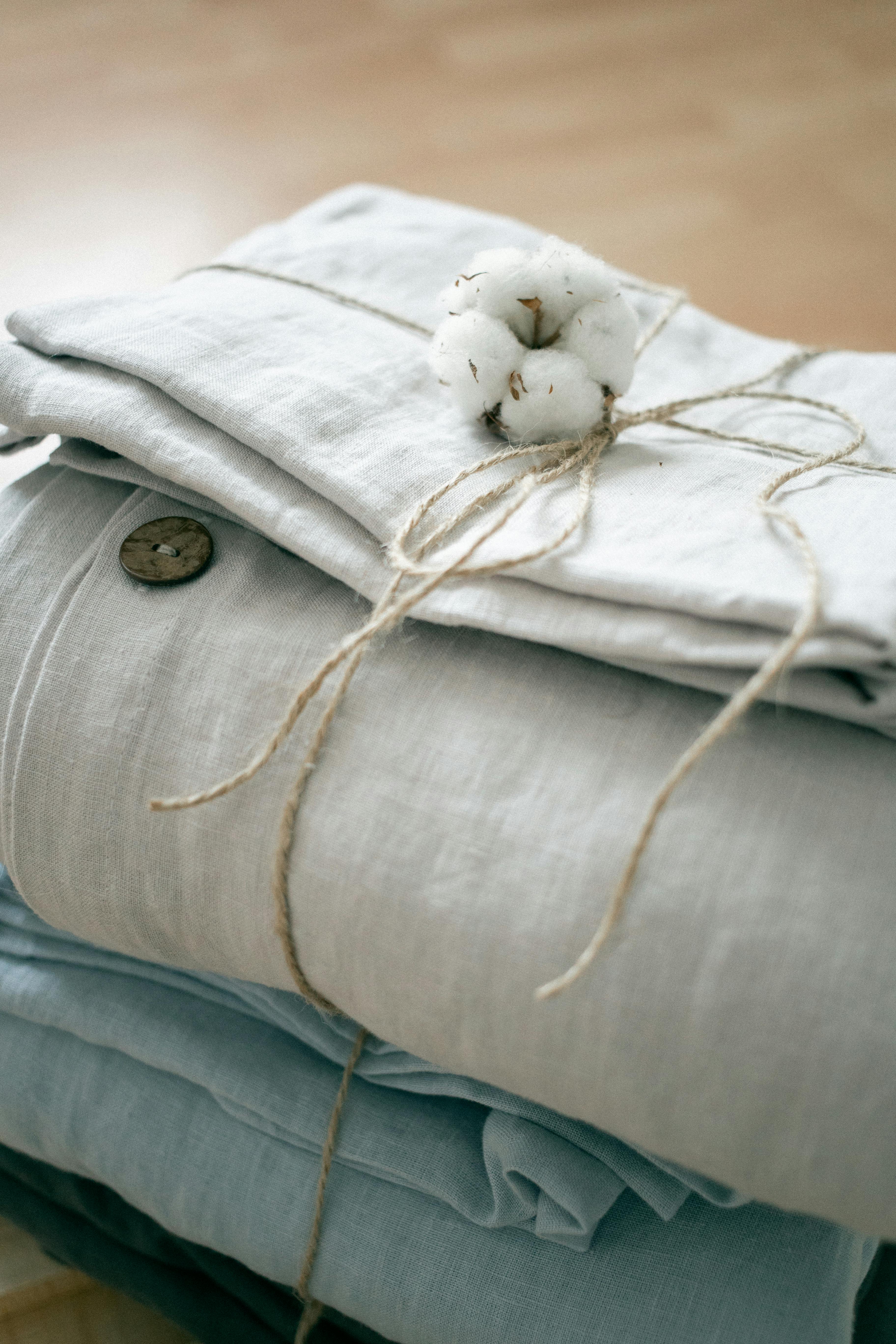 Three stacked button up natural fiber shirts, individually folded and tied with twine on a wooden surface.