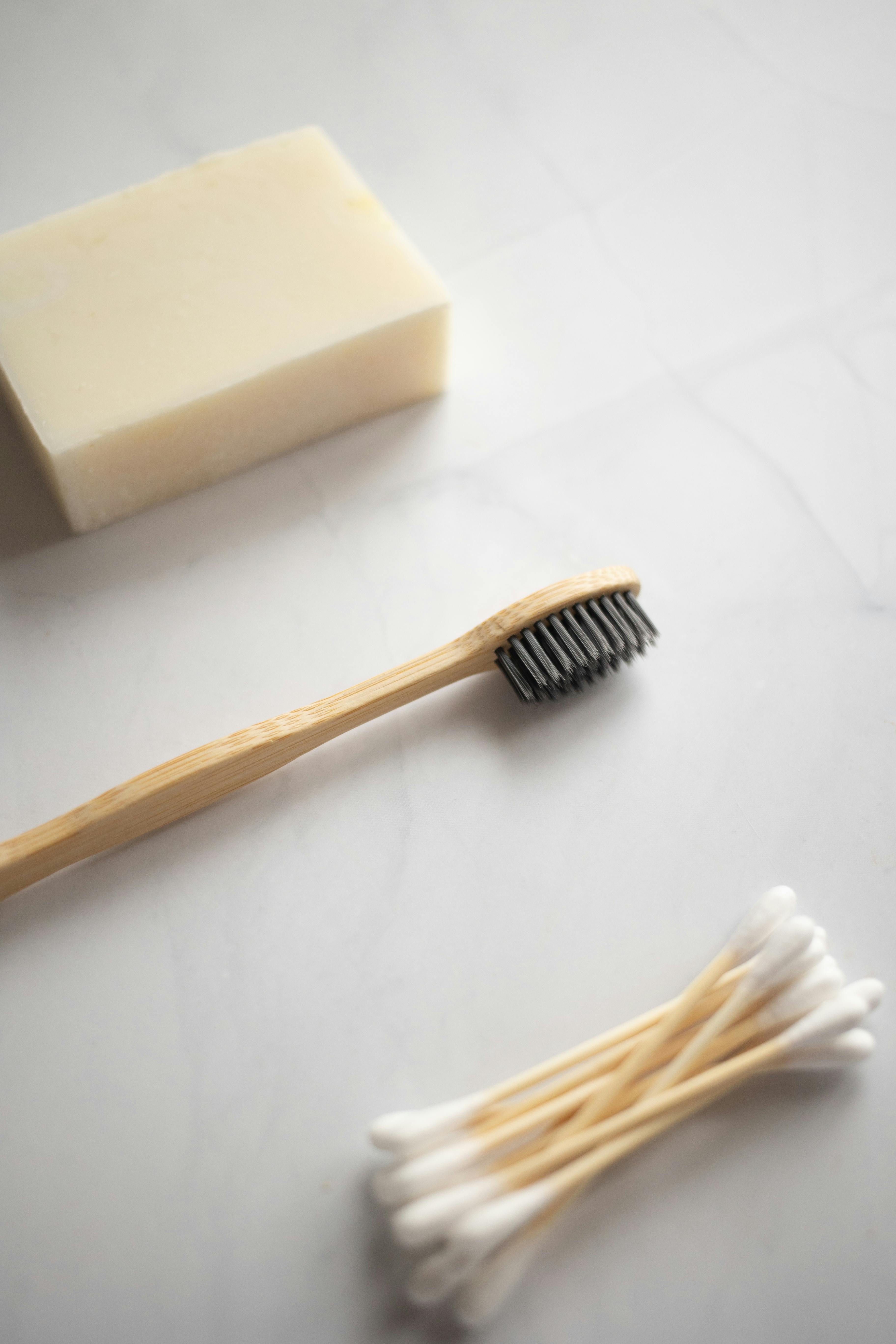 A bar of soap, toothbrush and cotton swabs placed on a white counter top.