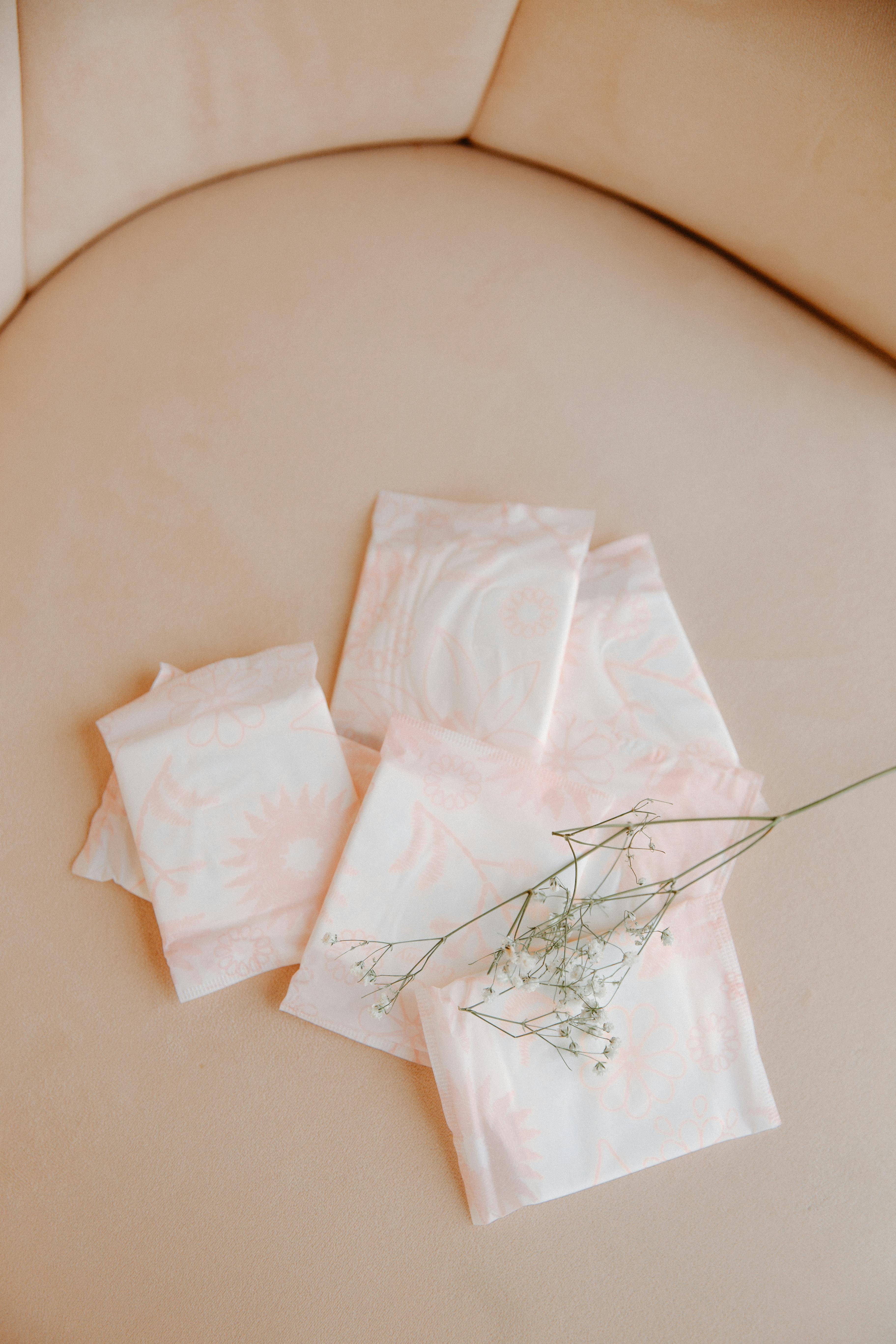 Six packaged biodegradable sanitary pads on a pink surface