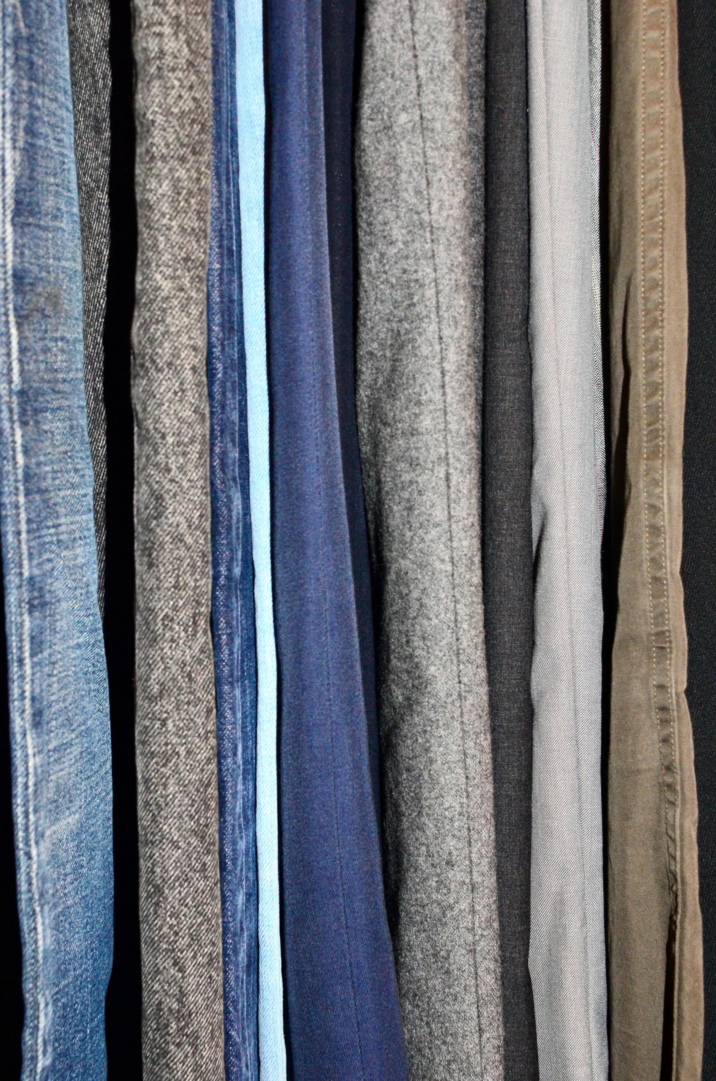 Multiple pants of different colors and textures hanging in a vertical position.