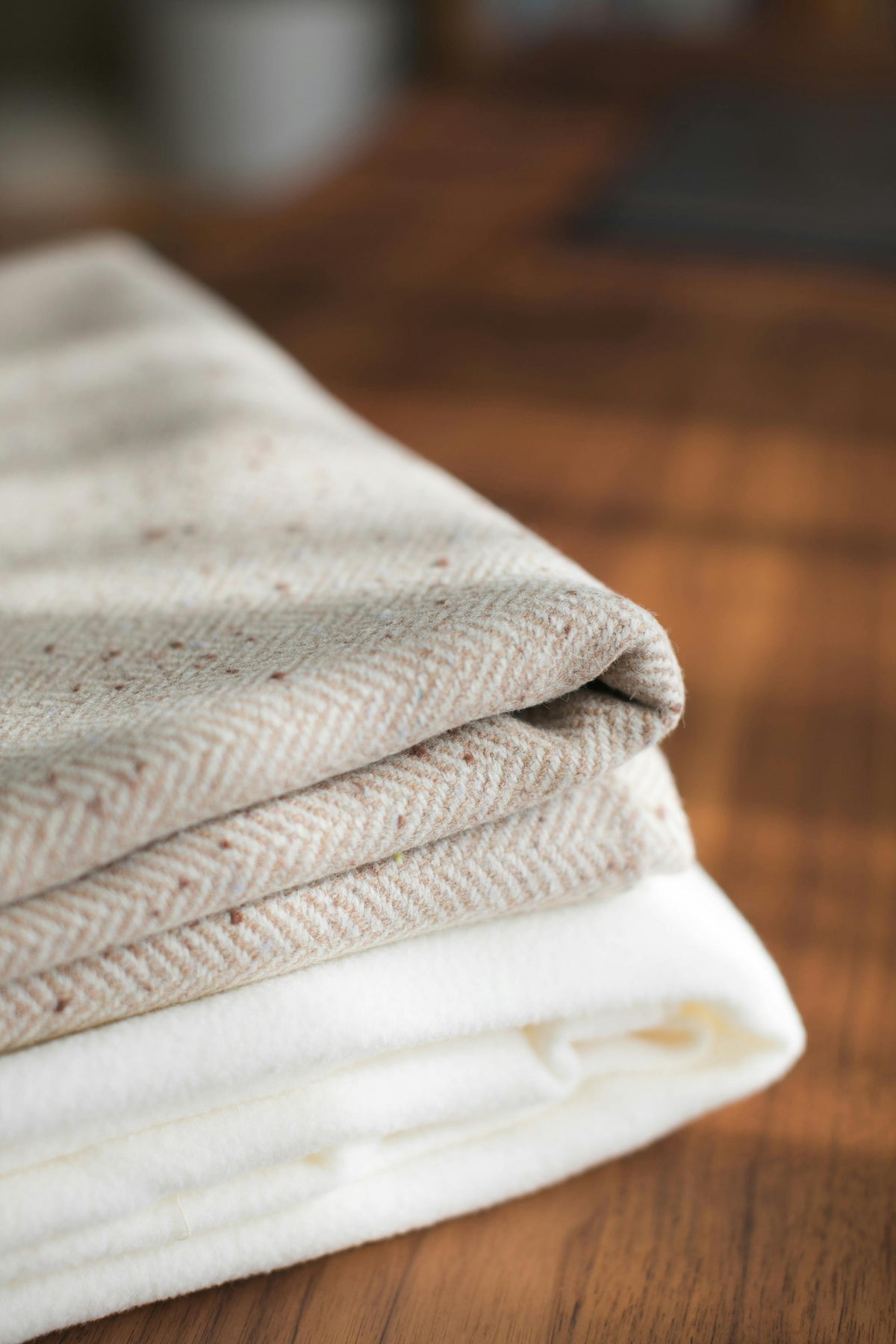 White and beige folded linen sheets stacked on a wooden surface.