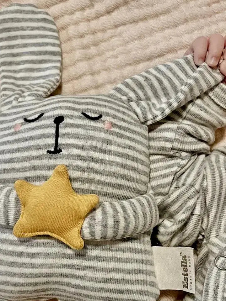 Child wearing a striped outfit holding a striped plush toy with a yellow star on a textured blanket in the background.