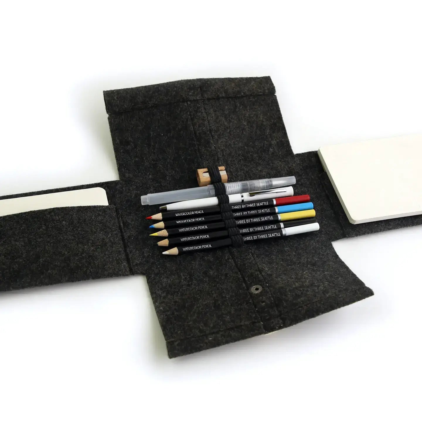 Dark gray felt pencil case with water color pencils and a notebook on a white background