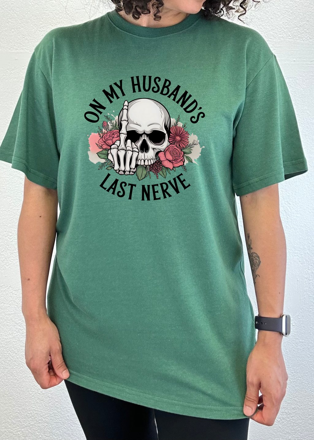 Person wearing a green t-shirt with a skull and text 'On my husband's last nerve' design on a white background