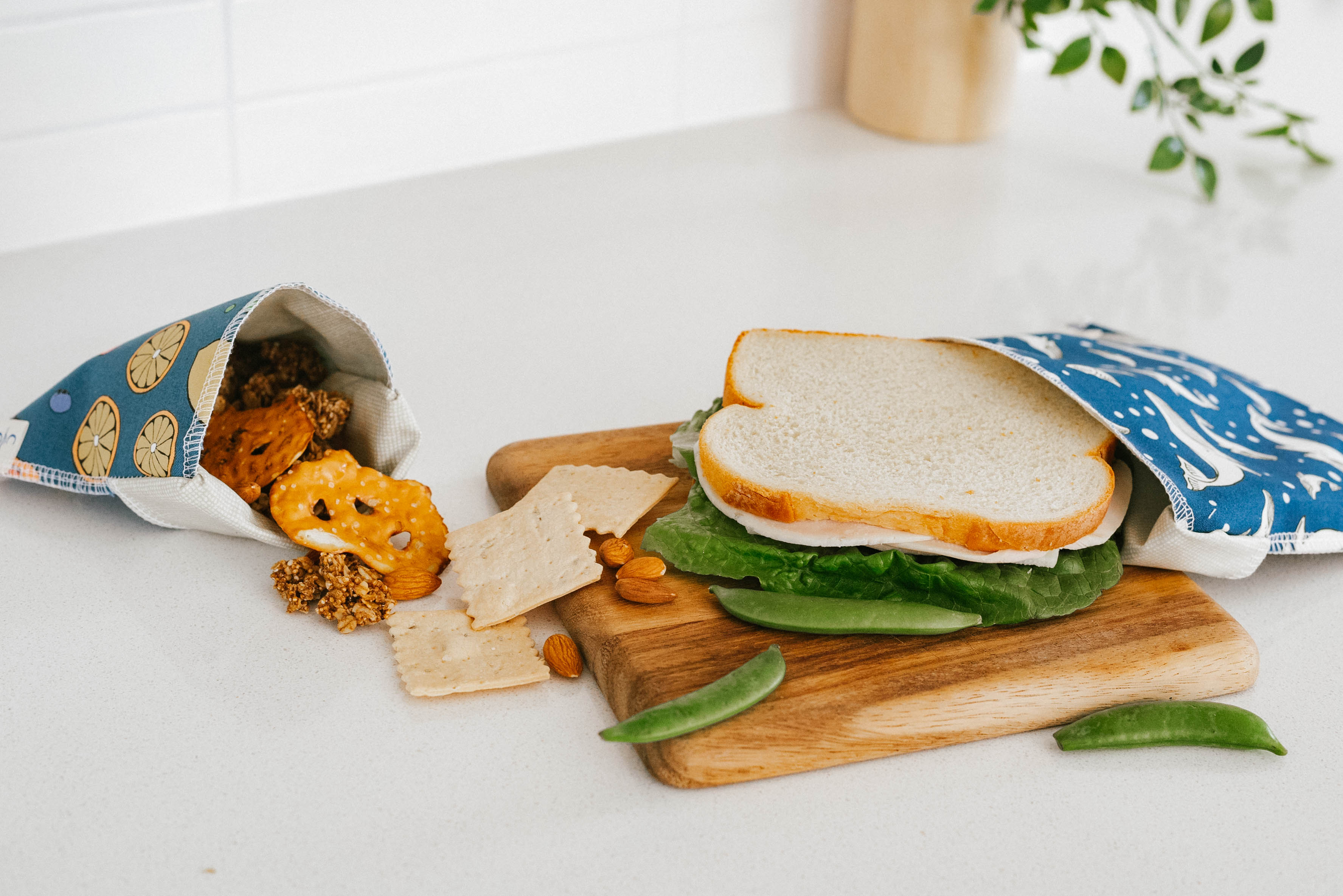 Sandwich on a wooden board with snacks on a white surface