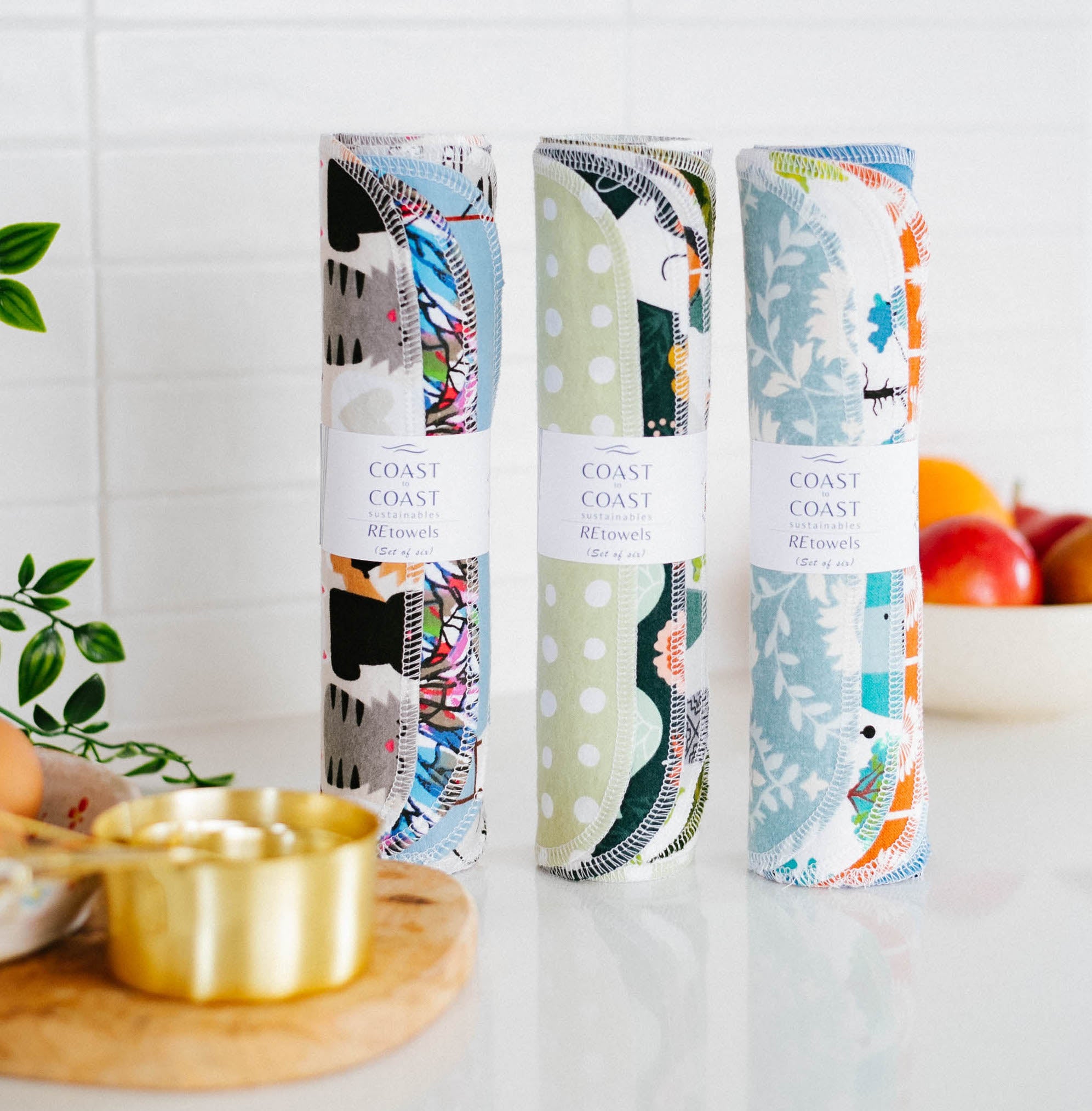 Three sets of colorful rolled-up, soft flannel fabric towels, with 'Coast to Coast' branding on a kitchen counter.