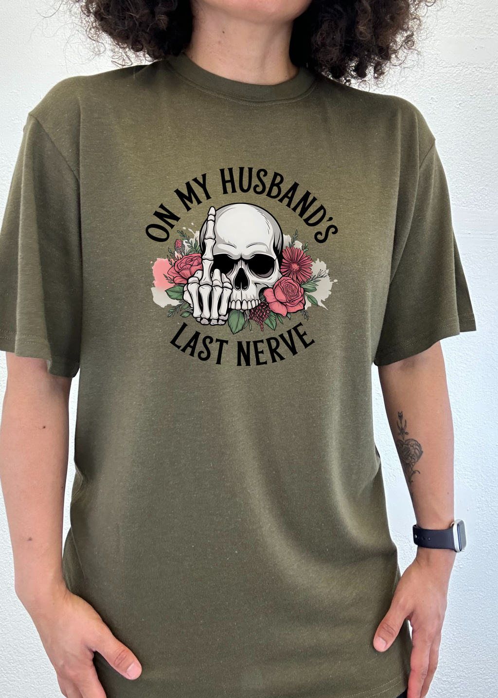 Person wearing a green t-shirt with a skull design and text 'On my husband's last nerve'.