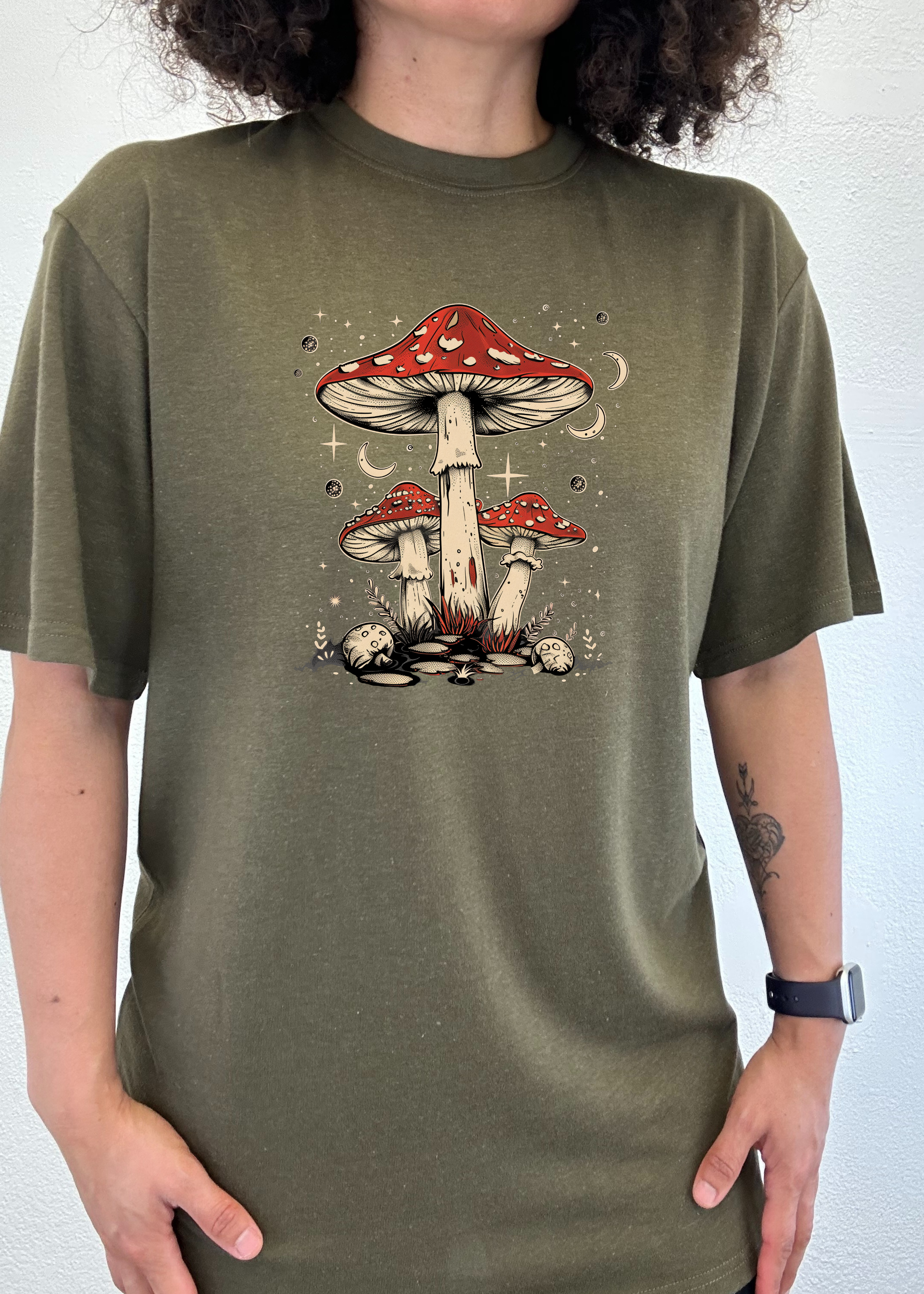 Person wearing a green t-shirt with a mushroom design on a plain background