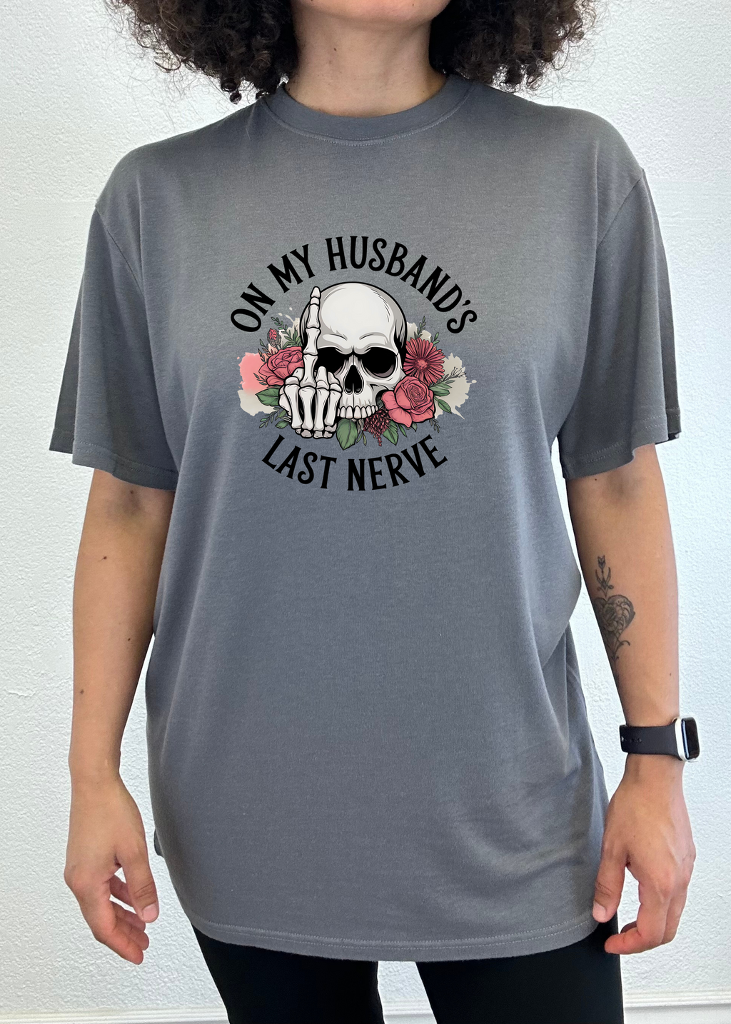 Person wearing a gray t-shirt with a skull and text 'On my husband's last nerve' design on a white background