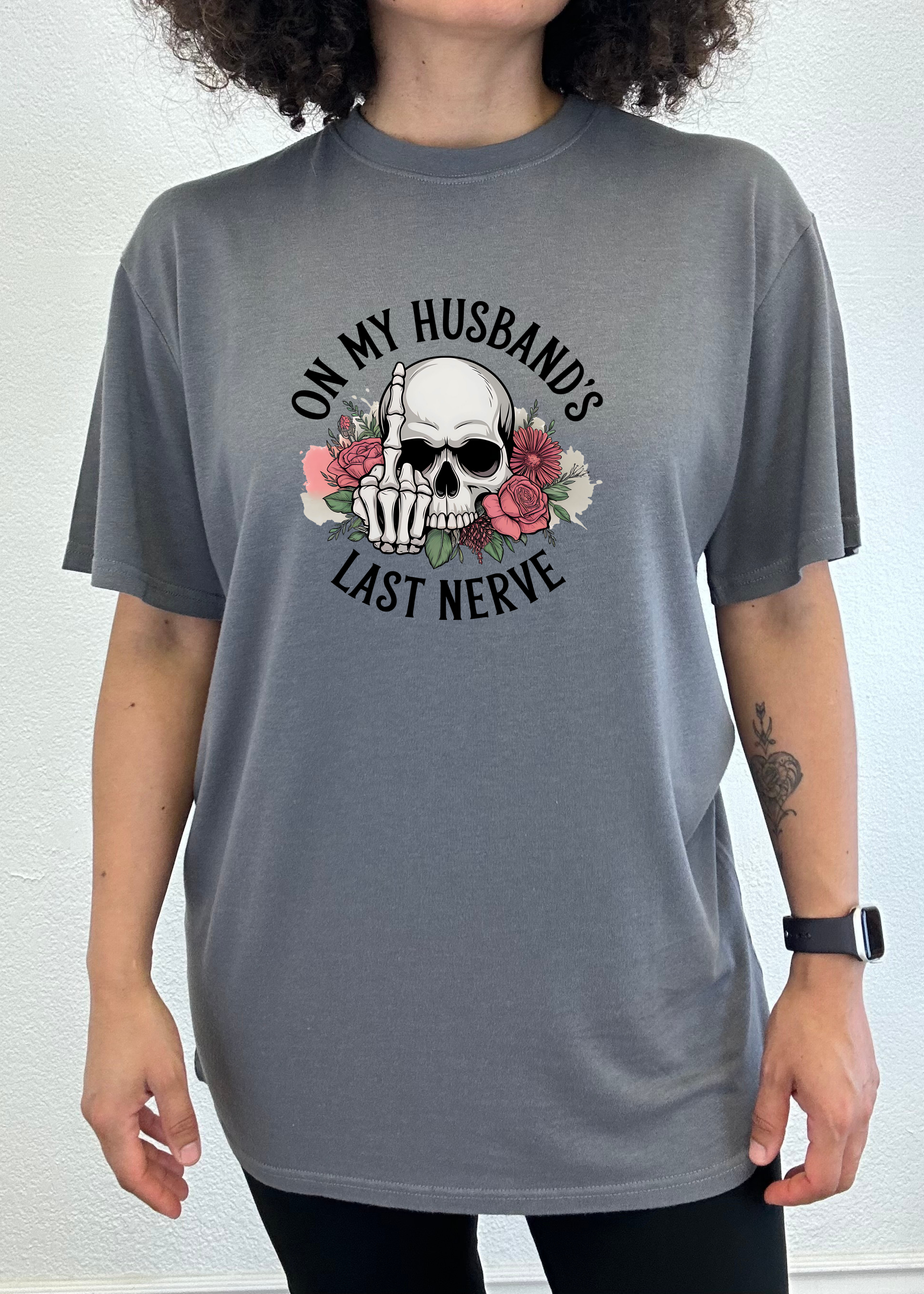 Person wearing a gray t-shirt with a skull and text 'On my husband's last nerve' design on a white background