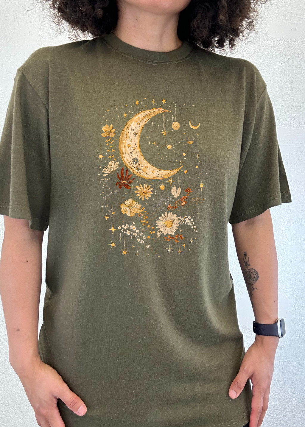 Person wearing a green t-shirt with a celestial design featuring a crescent moon and flowers.
