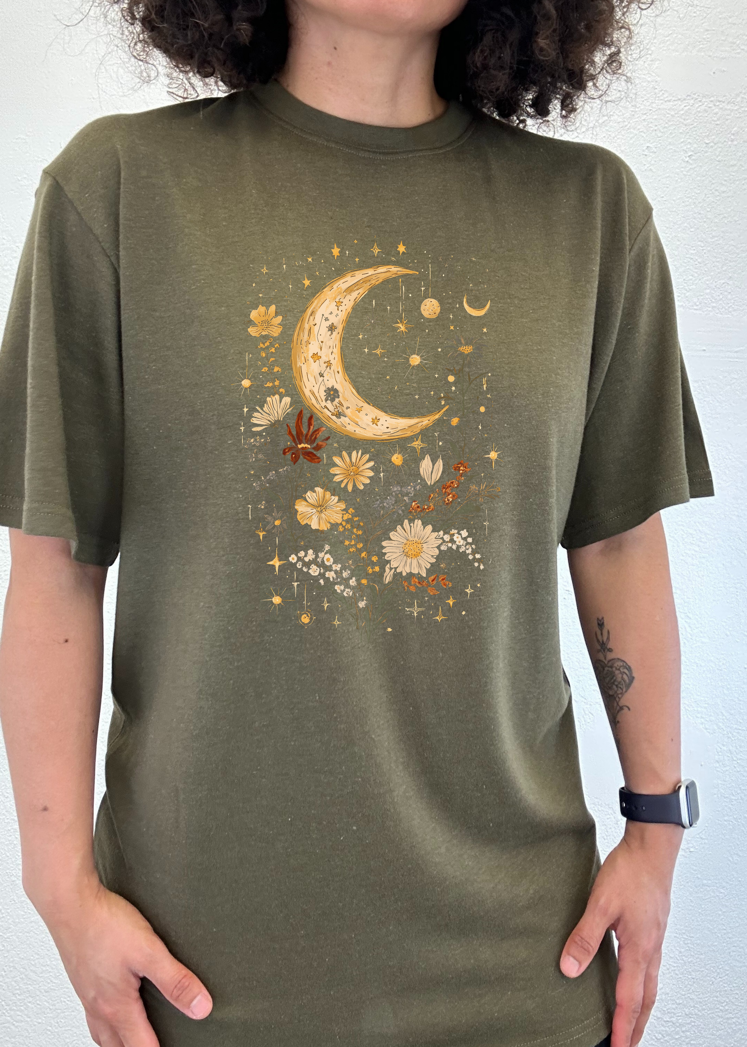 Person wearing a green t-shirt with a celestial design featuring a crescent moon and flowers.