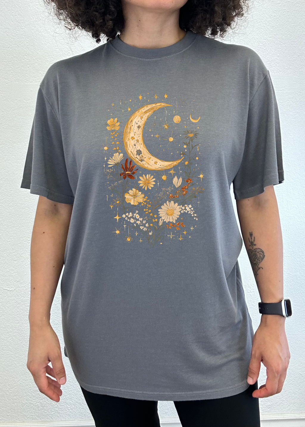 Person wearing a gray t-shirt with a celestial design featuring a moon and flowers.