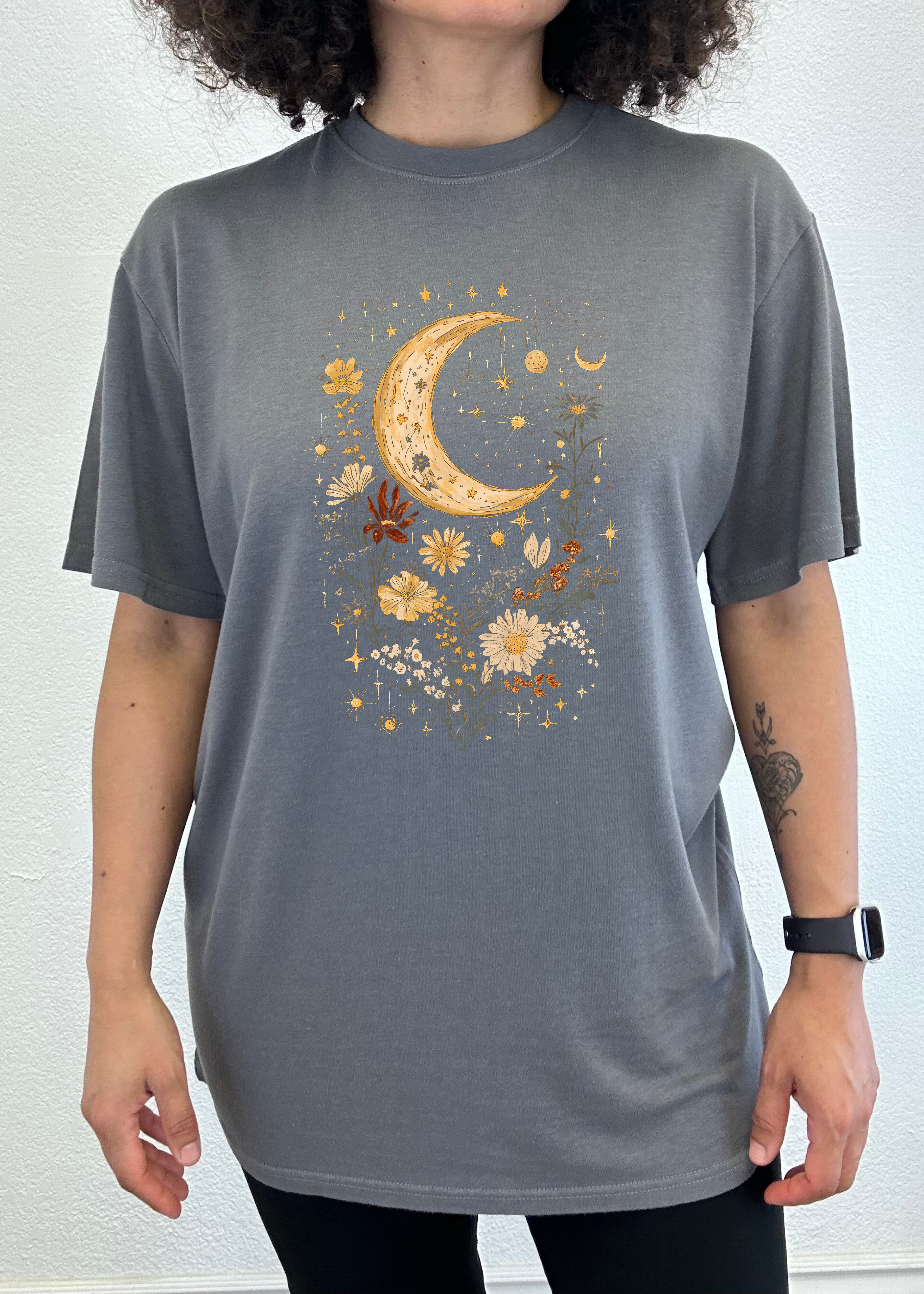Person wearing a gray t-shirt with a celestial design featuring a moon and flowers.