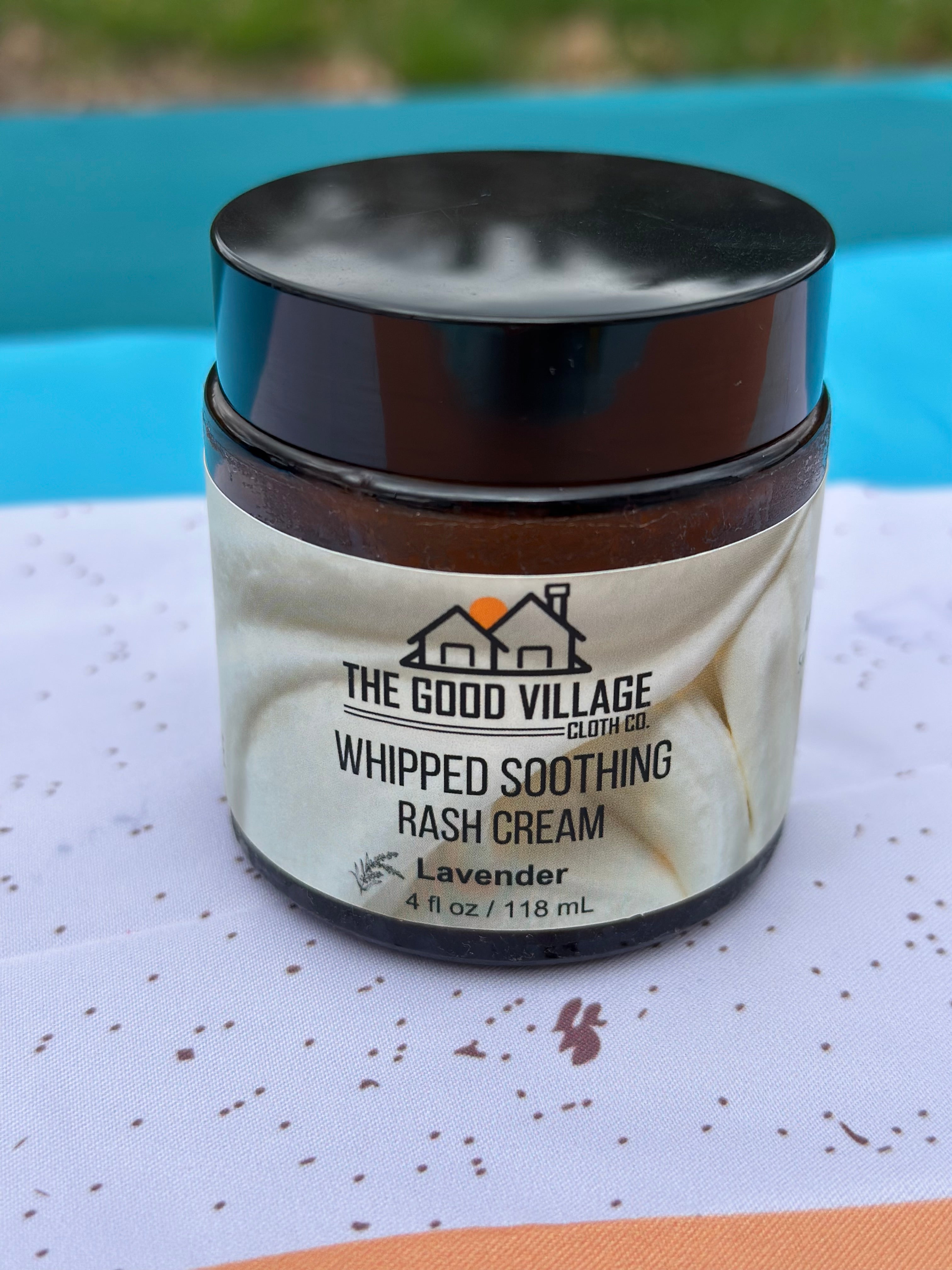Jar of 'Whipped Soothing Rash Cream' by The Good Village on a textured surface with a blurred background