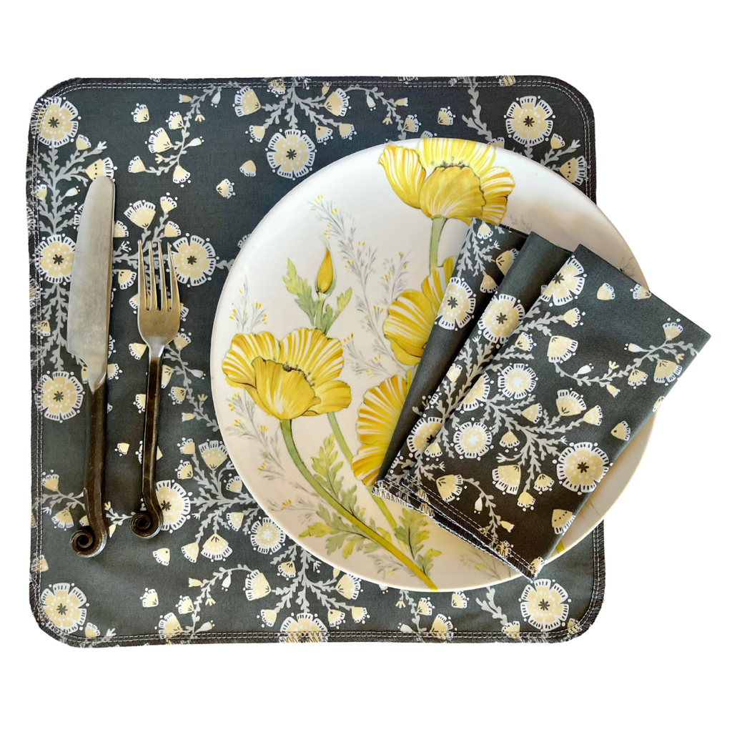 Dinner set with floral design on placemat, plate, knife, fork, and napkin.