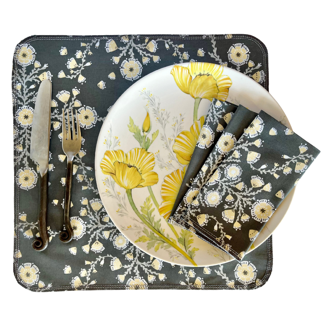Dinner set with floral design on placemat, plate, knife, fork, and napkin.