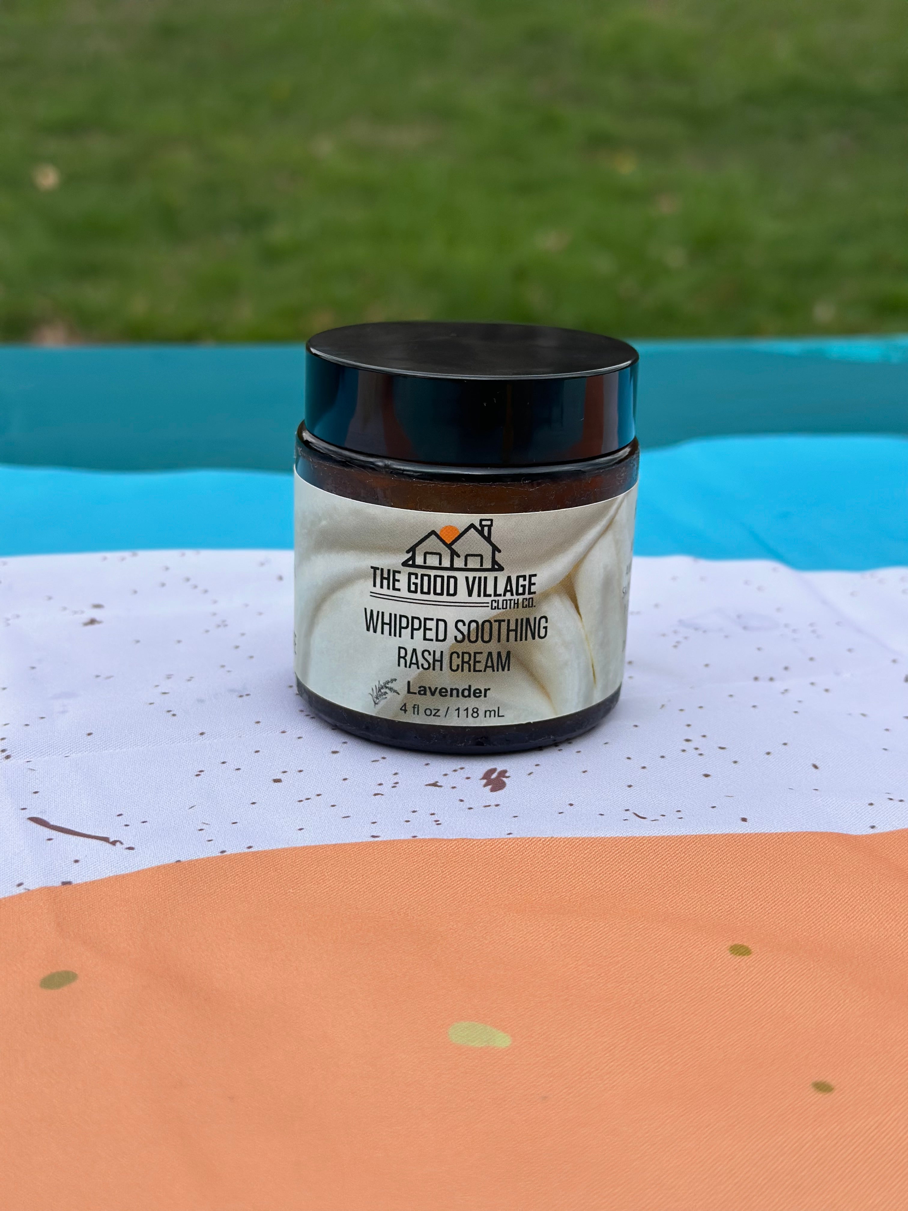 Jar of 'The Good Village' whipped soothing rash cream on a colorful surface with grass in the background