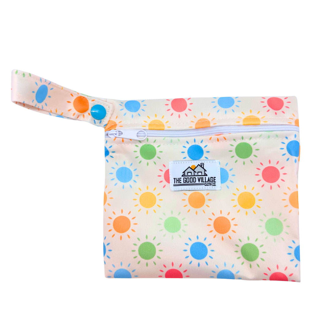 Colorful pouch with sun pattern and 'The Good Village' logo on a white background