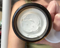 Close-up of a jar of white cream held by a person.