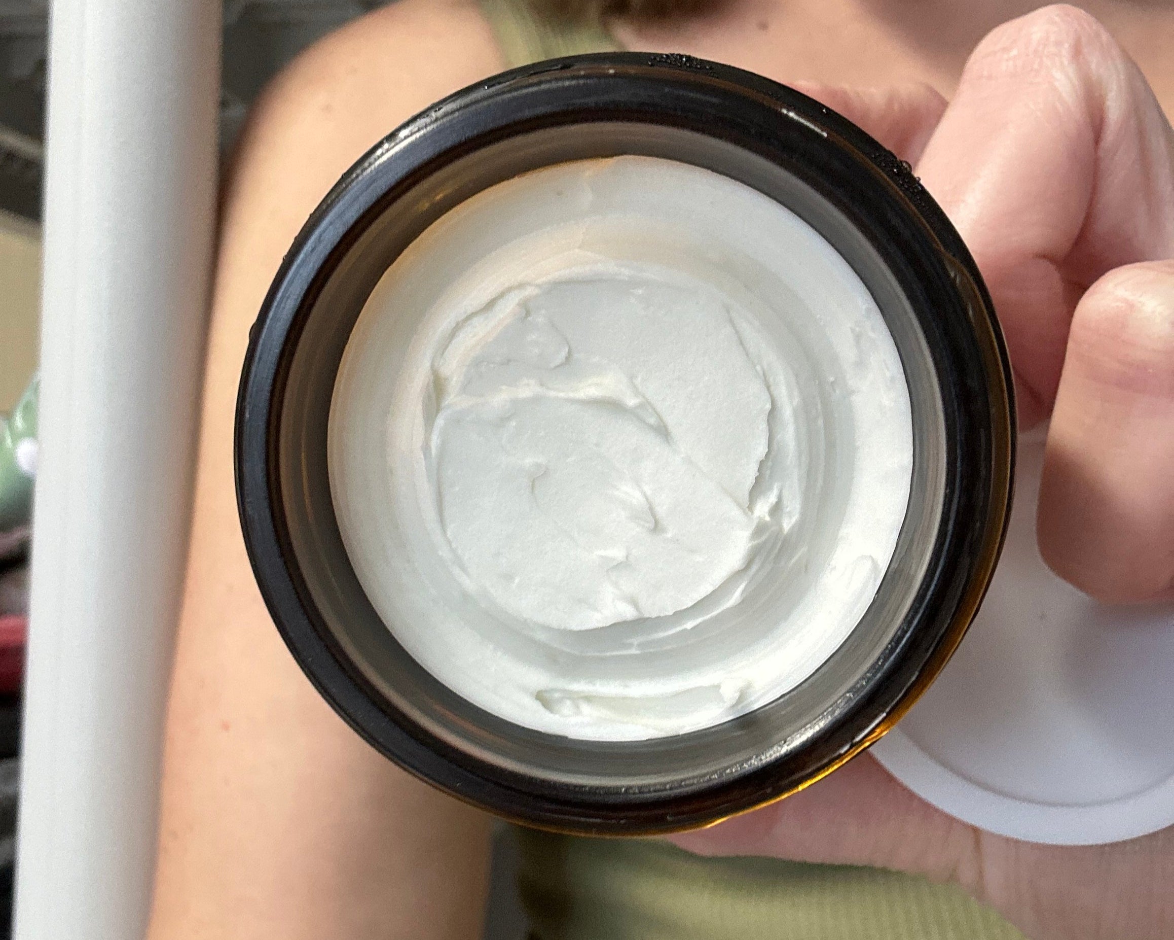 Close-up of a jar of white cream held by a person.