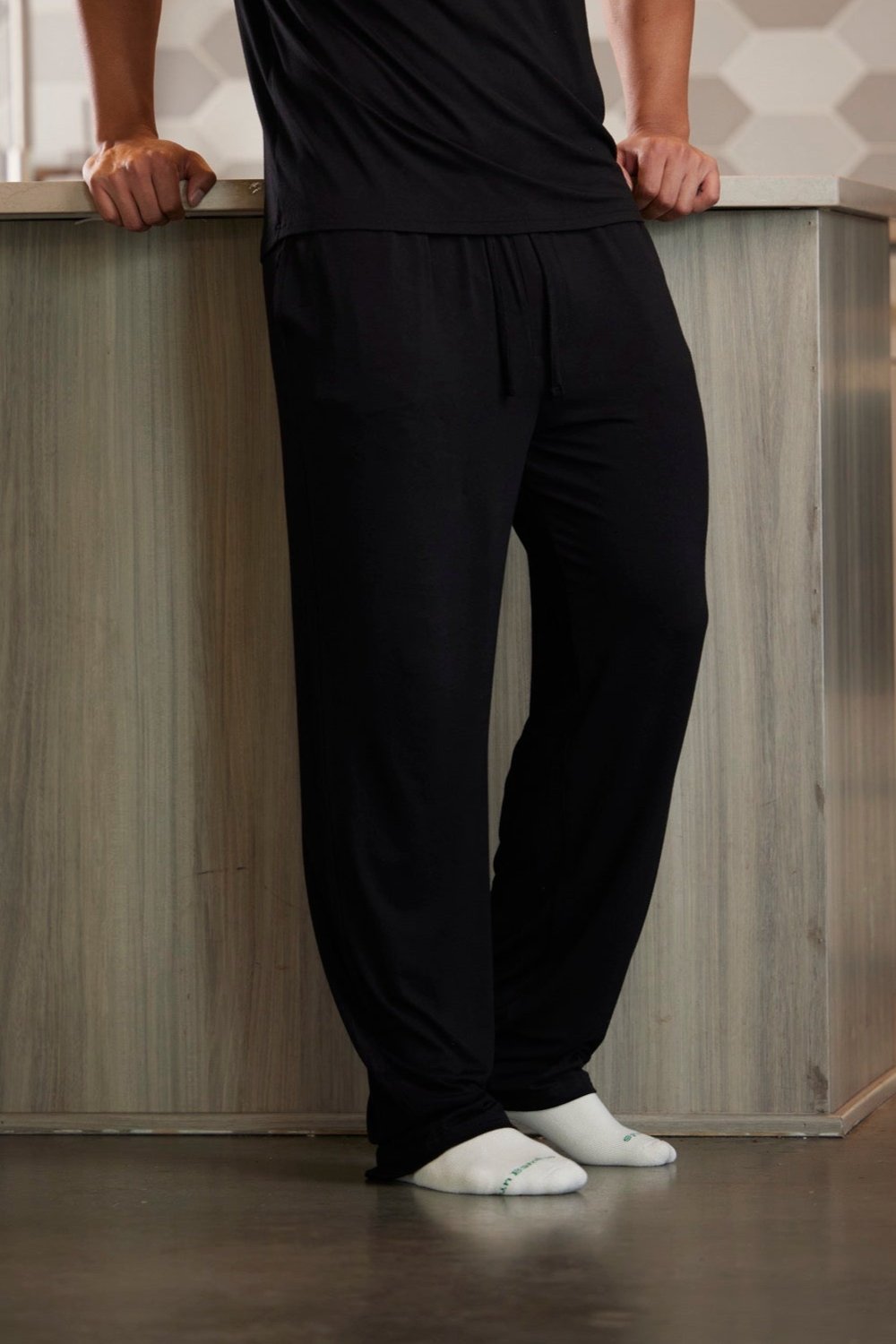 Person wearing black pants and white socks standing against a wooden panel background