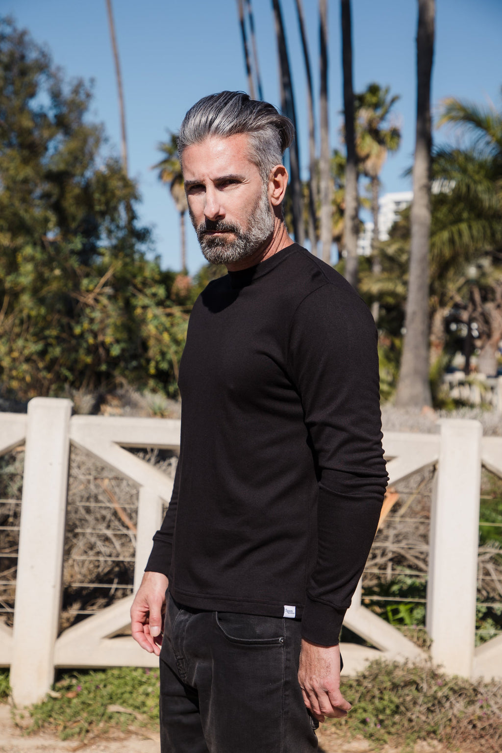 Man wearing a black long-sleeve shirt standing outdoors with palm trees in the background