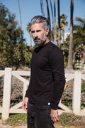 Man wearing a black long-sleeve shirt standing outdoors with palm trees in the background