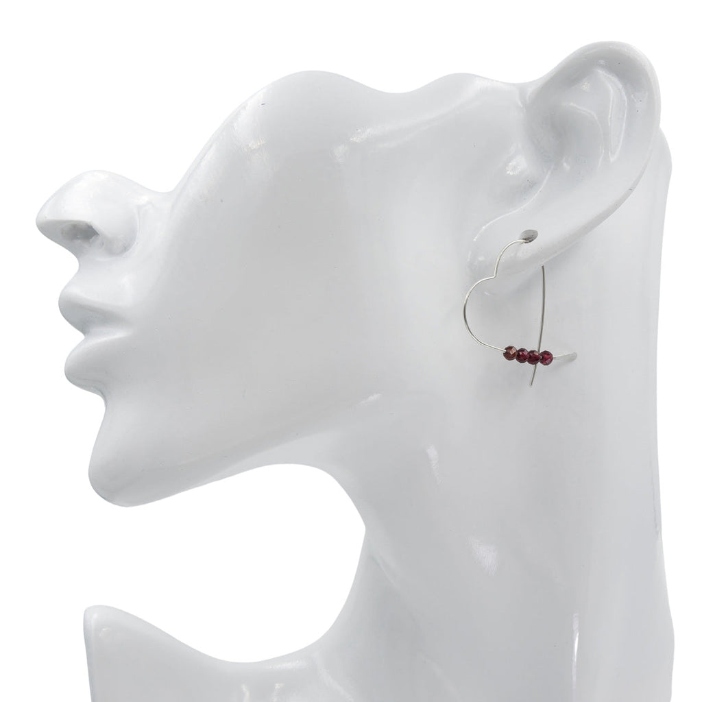 Silver heart shaped earring on a white mannequin ear with a plain background