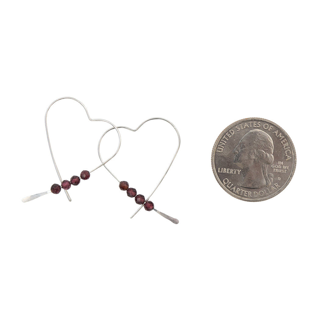 Heart-shaped earrings with beads next to a quarter for scale on a white background