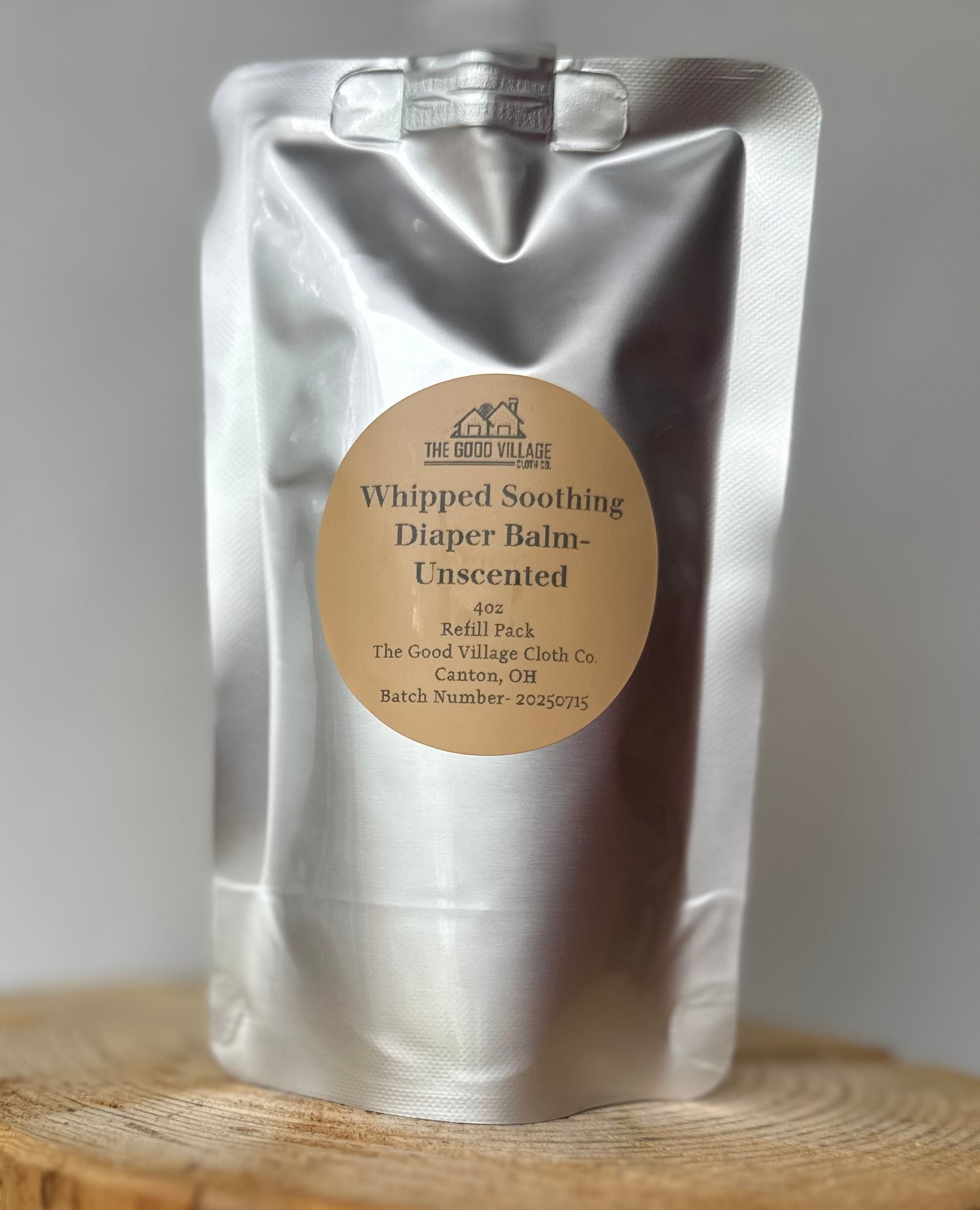 Silver packaging of 'Whipped Soothing Diaper Balm Unscented' with a label on a wooden surface.