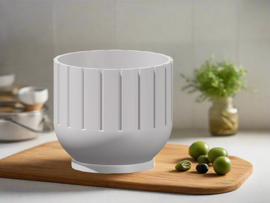 White planter on a wooden cutting board with green olives and a blurred kitchen background
