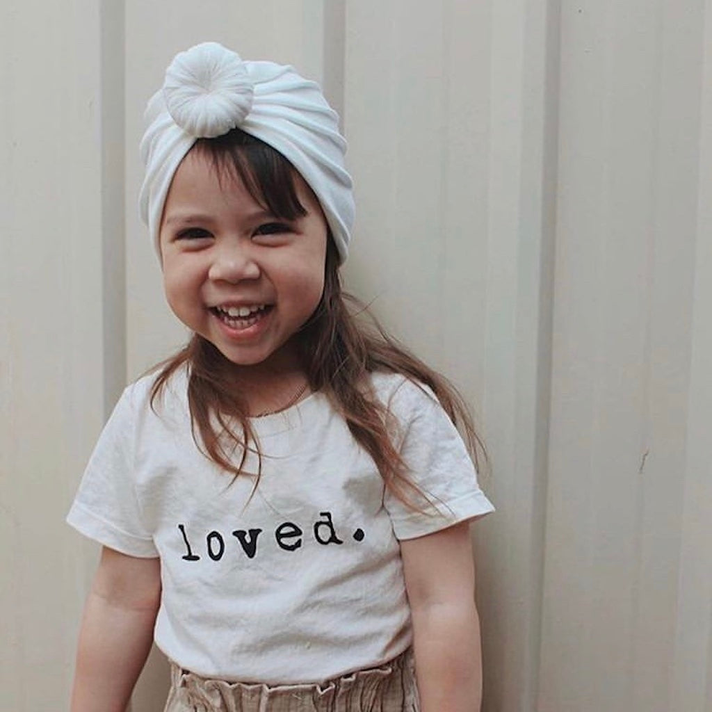 Child wearing a white t-shirt with 'loved.' text and a white headband against a plain background