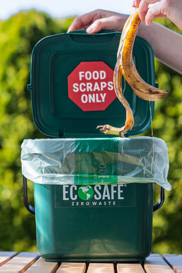 Person disposing of a banana peel into an 'ECO-SAFE' zero waste bin with a 'Food Scraps Only' sign.