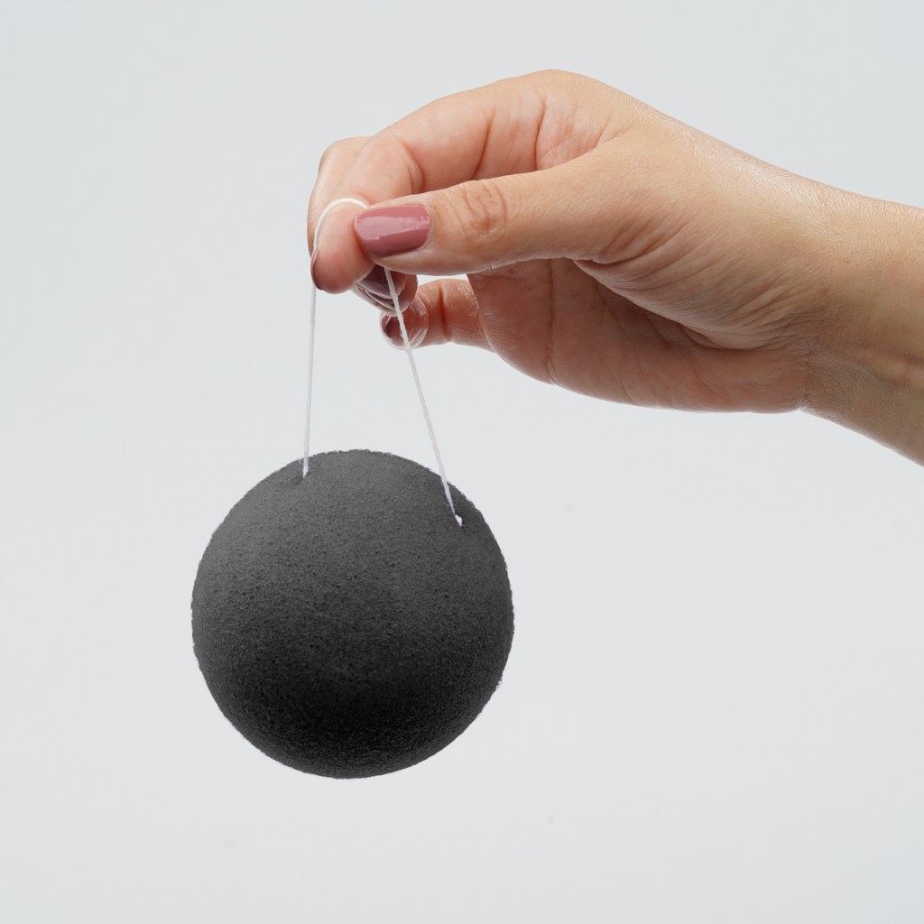 Hand holding a black konjac sponge on a white background