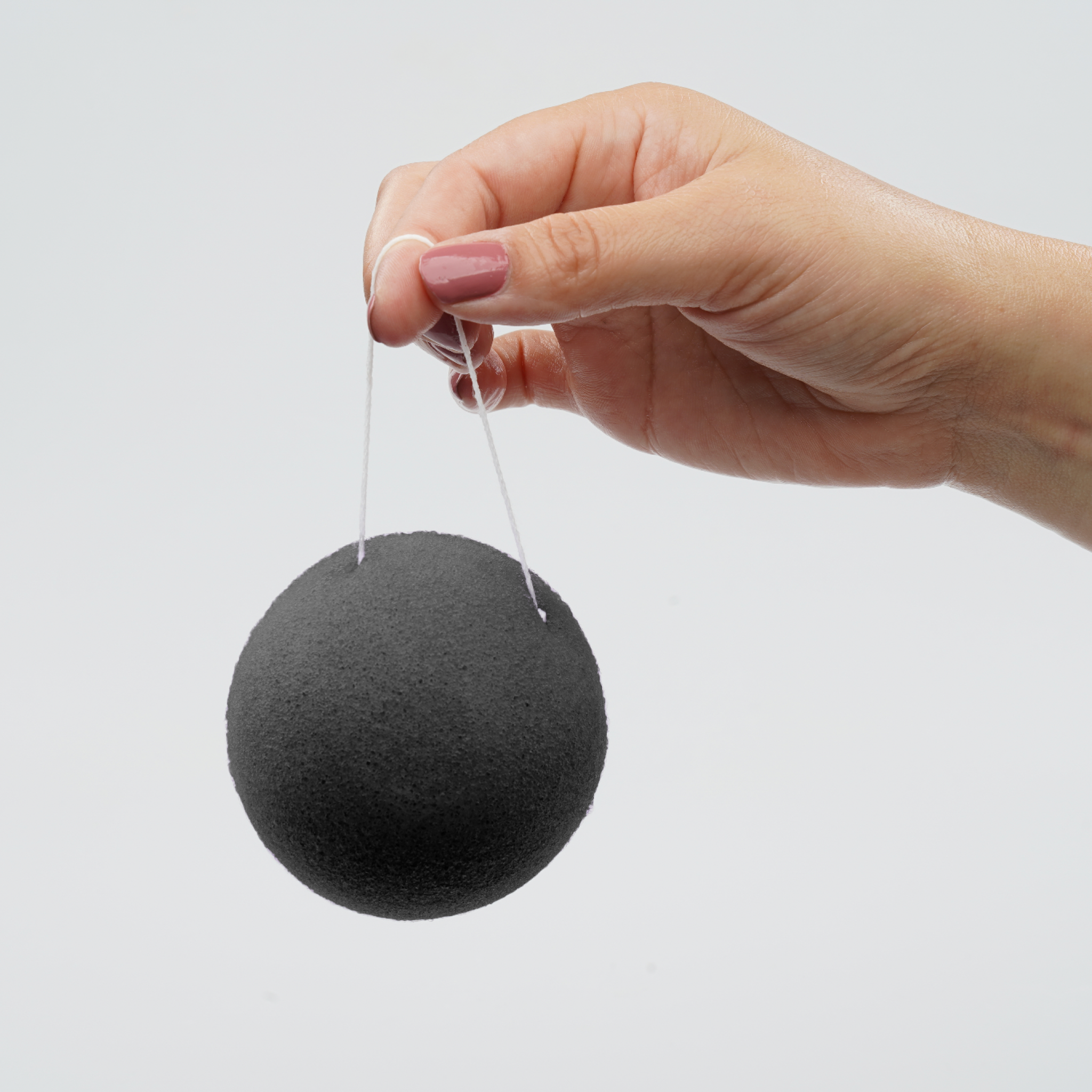 Hand holding a black konjac sponge on a white background