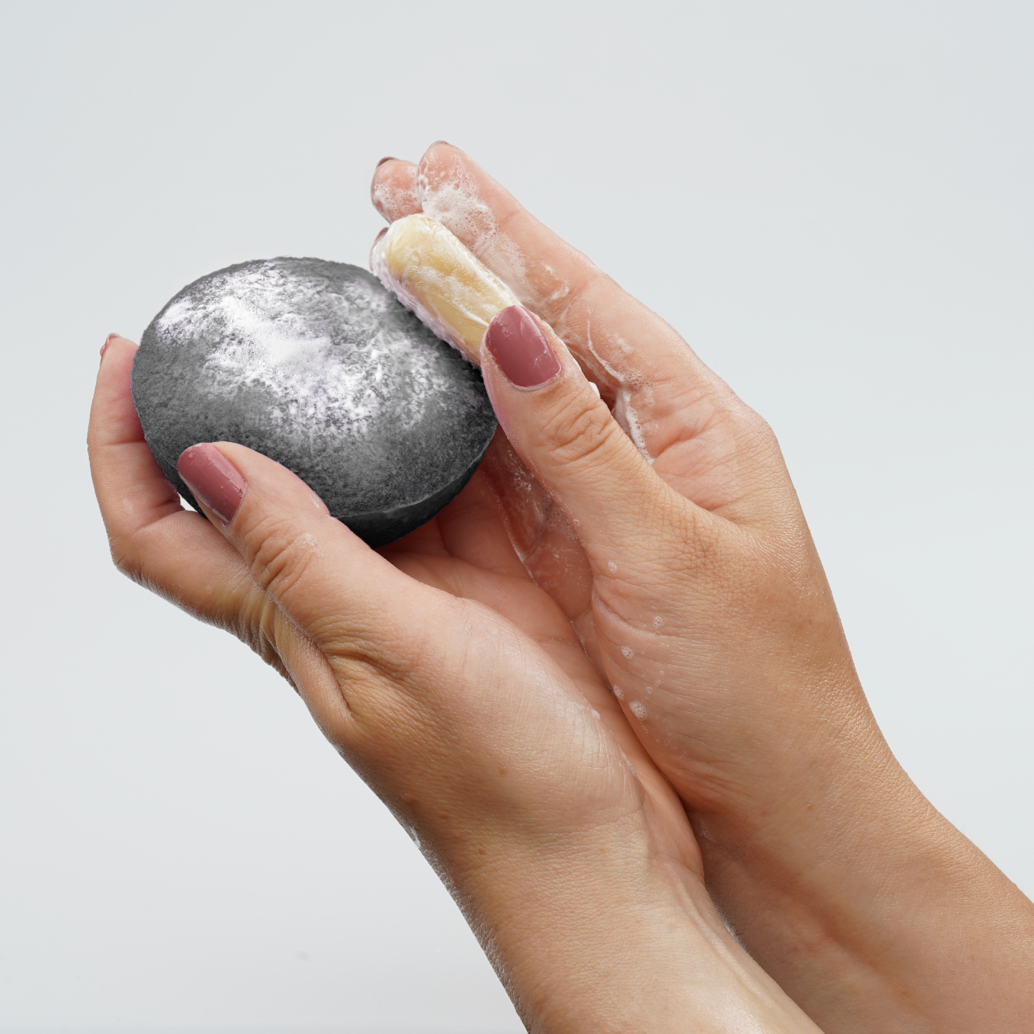 Person holding a dark gray sponge and soap bar with soapy lather on a light gray background