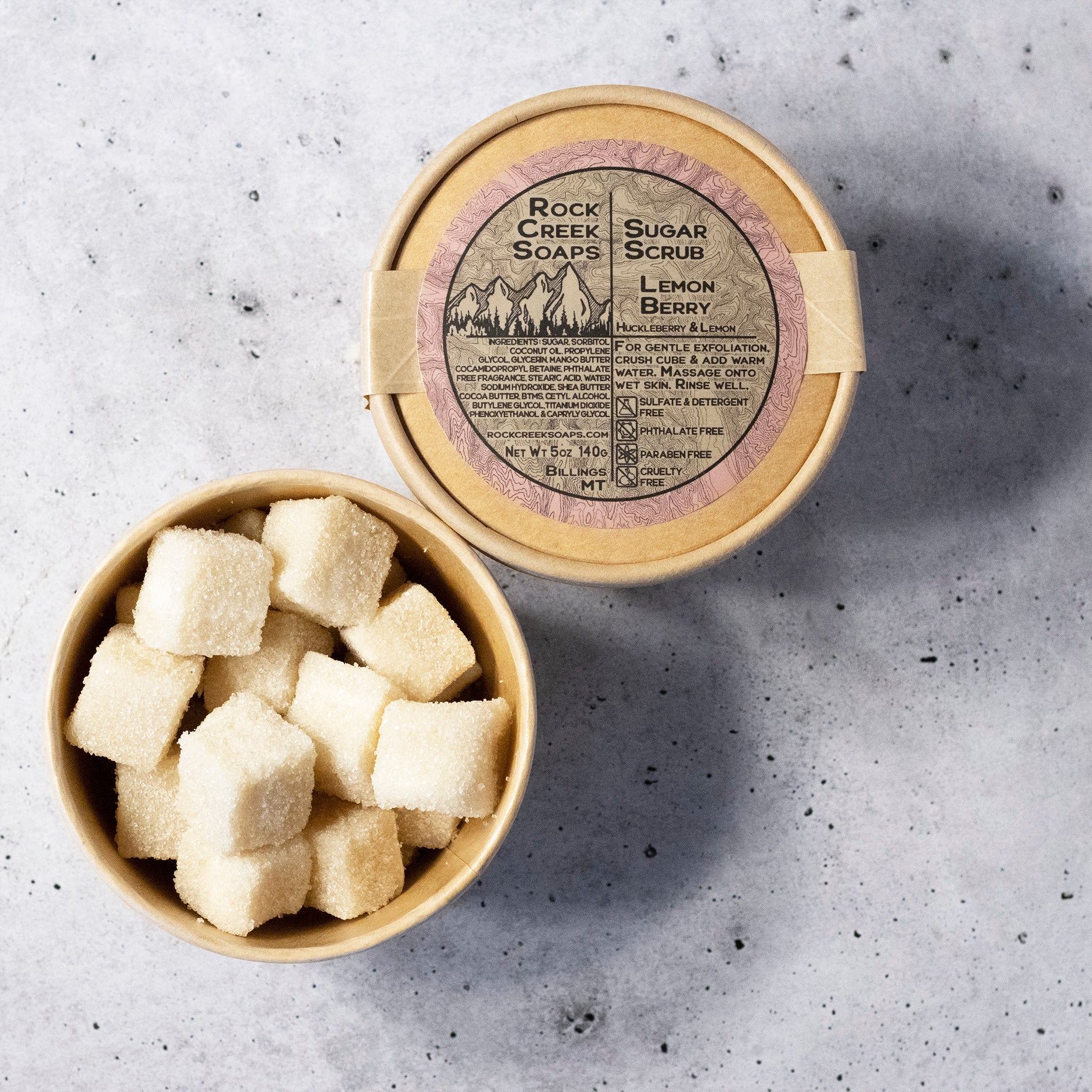 Rock Creek Soaps Lemon Berry sugar scrub with open container on a gray surface