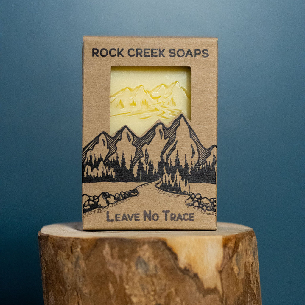 Rock Creek Soaps 'Leave No Trace' soap bar with mountain design on a wooden block against a blue background