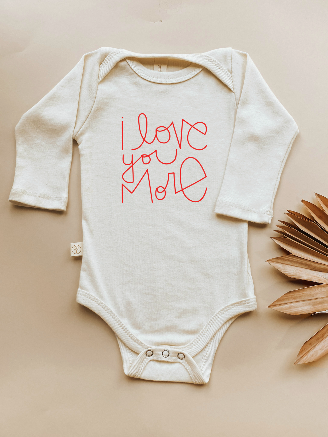 White baby onesie with 'I love you more' text in red on a beige background
