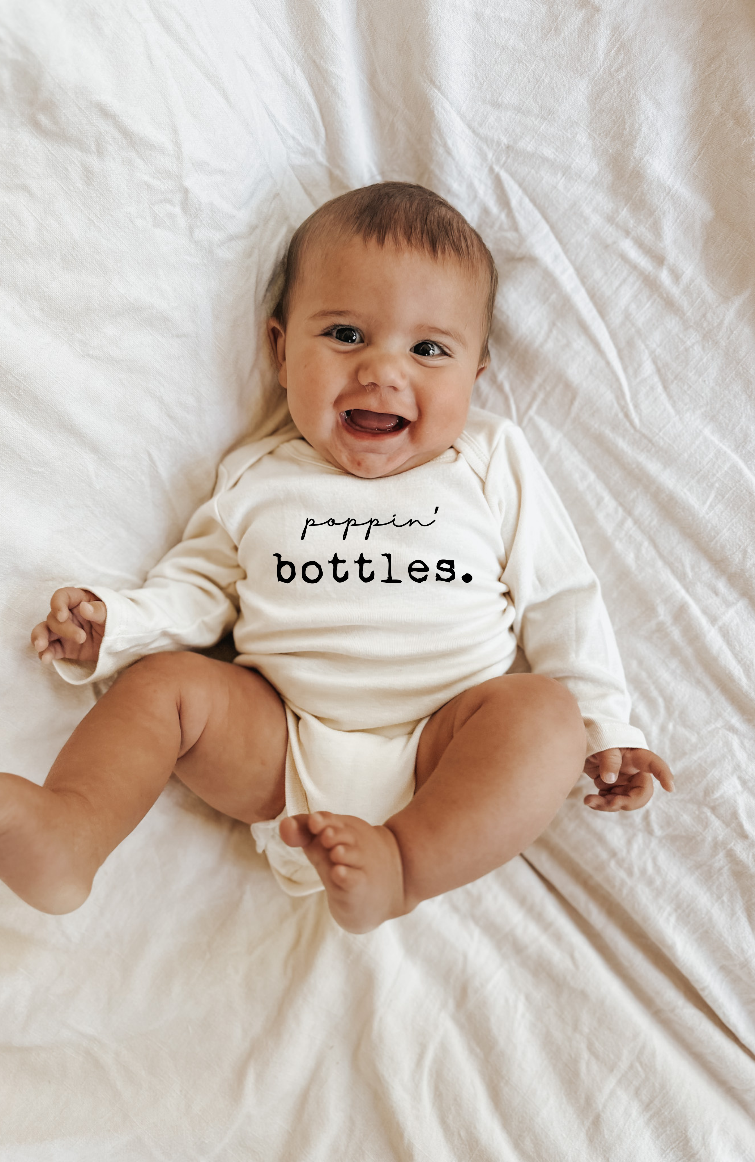 Baby wearing a onesie with 'poppin bottles.' text on a white blanket
