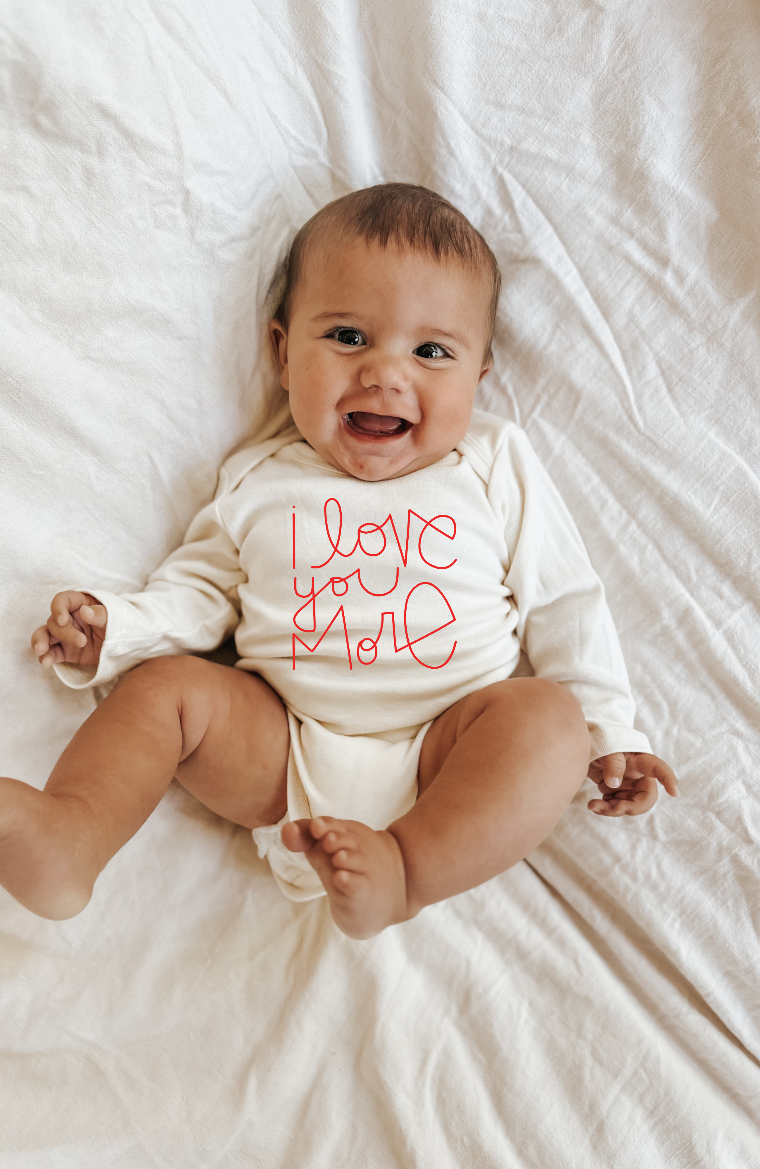 Baby wearing a onesie with 'I love you more' text on a white blanket