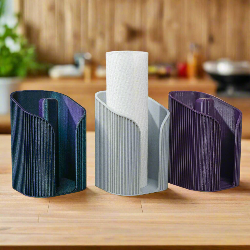 Three paper towel holders in black, gray, and purple on a wooden surface with a kitchen background.