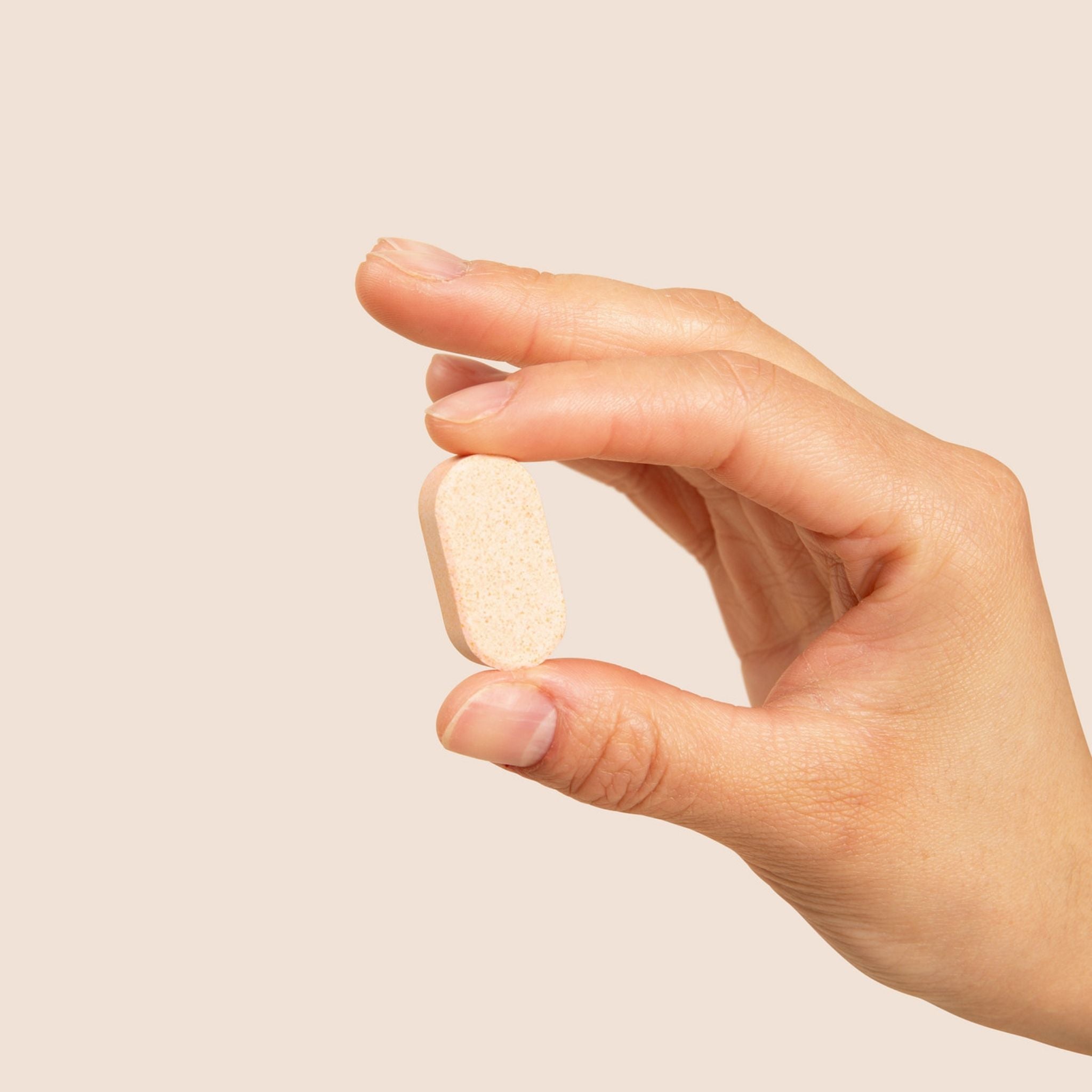 Hand holding a beige pill against a plain background