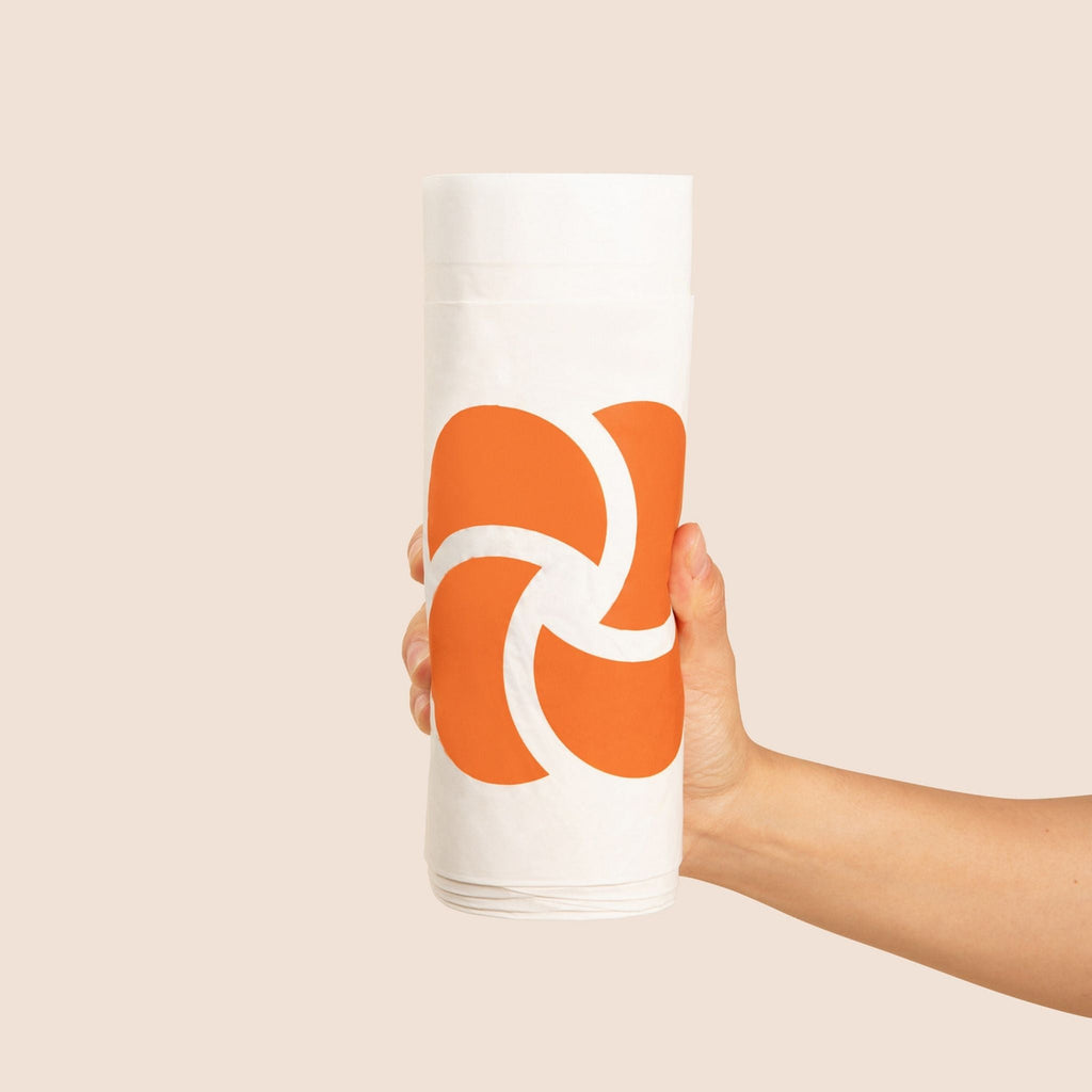 Hand holding a roll of waste bags with an orange and white logo against a beige background