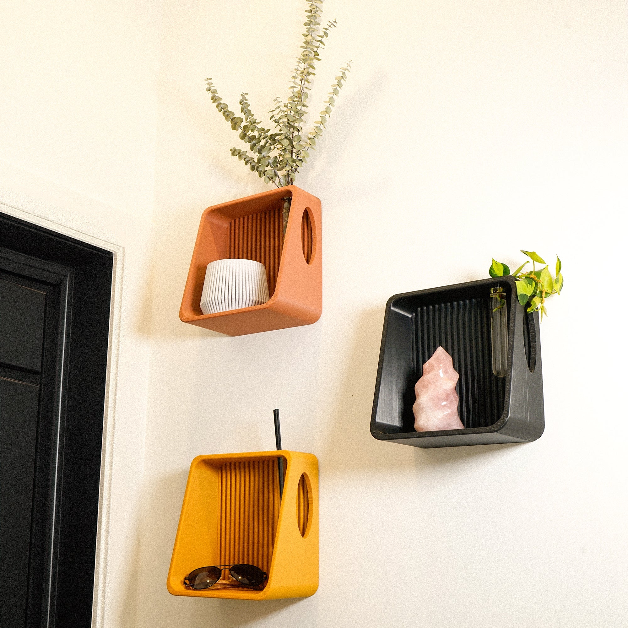 Three wall-mounted shelves in orange, black, and yellow with decorative items on a white wall.