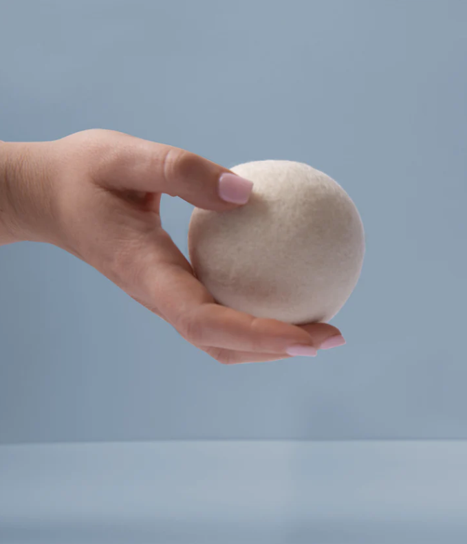 Hand holding a white dryer ball against a light blue background