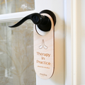 Light wood door handle hanger reading 'Therapy In Practice' on a door.